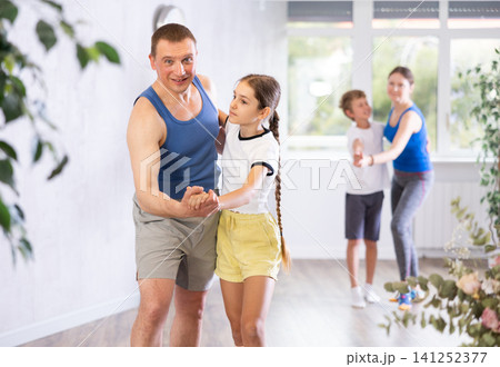 Active school girl practicing dance in pair with her sporty middle-aged father in dance hall during family training Active school girl practicing dance in pair with her sporty middle-aged father in dance hall during family training 141252377