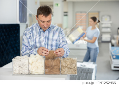 Interested man examining fillings for upholstered furniture in showroom Interested man examining fillings for upholstered furniture in showroom 141252433