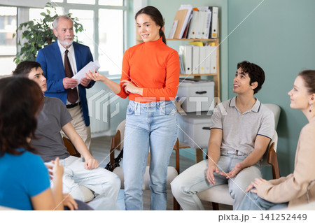 Young girl standing and talking to students sitting in a circle Young girl standing and talking to students sitting in a circle 141252449
