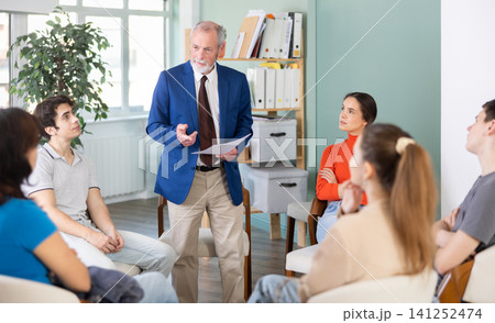 Youth girls and guys sit at circle, listen to senior man coach. 141252474