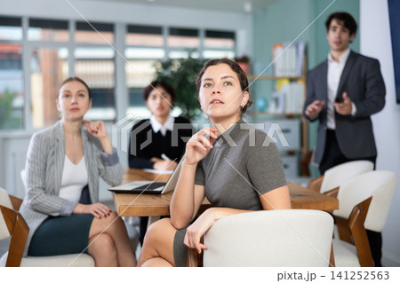 Interested malaysian girl office worker sitting at table with group of people and watching presentation during business meeting in office Interested malaysian girl office worker sitting at table with group of people and watching presentation during business meeting in office 141252563