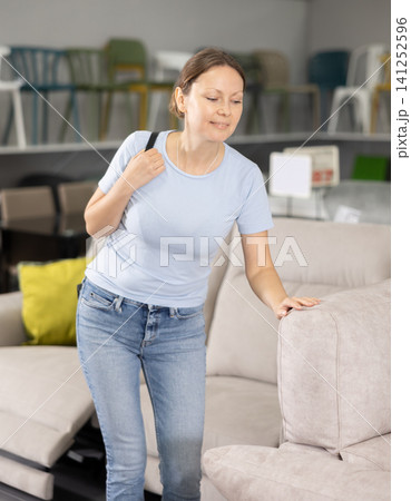 Woman in store inspects upholstered furniture. Woman in store inspects upholstered furniture. 141252596