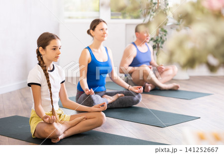 Pleasant preteen girl practicing lotus pose of yoga with her family Pleasant preteen girl practicing lotus pose of yoga with her family 141252667