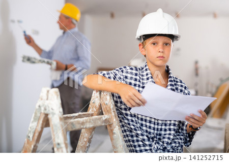 Portrait of young boy in hardhat with documents in building site Portrait of young boy in hardhat with documents in building site 141252715