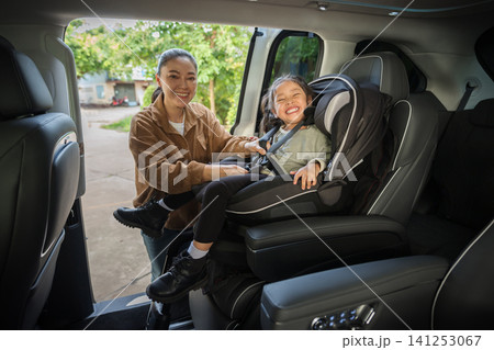 mother is fastening safety belt to preschool child girl in car seat, safety baby chair travelling mother is fastening safety belt to preschool child girl in car seat, safety baby chair travelling 141253067