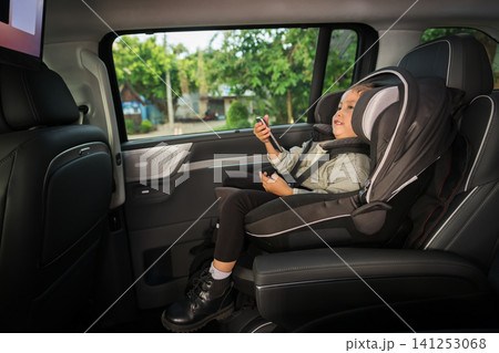 preschool child girl watching rear entertainment screen or ceiling screen while sitting in car seat, safety baby chair travelling preschool child girl watching rear entertainment screen or ceiling screen while sitting in car seat, safety baby chair travelling 141253068