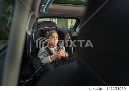 preschool child girl watching rear entertainment screen or ceiling screen while sitting in car seat, safety baby chair travelling preschool child girl watching rear entertainment screen or ceiling screen while sitting in car seat, safety baby chair travelling 141253069