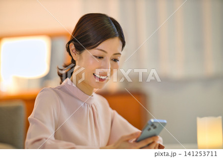 夜部屋でリラックスしてスマホを見る40代の女性 夜部屋でリラックスしてスマホを見る40代の女性 141253711