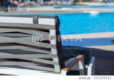 Modern outdoor lounge chair with gray woven straps placed beside a clear swimming pool, showcasing a serene and inviting leisure setting 141254512