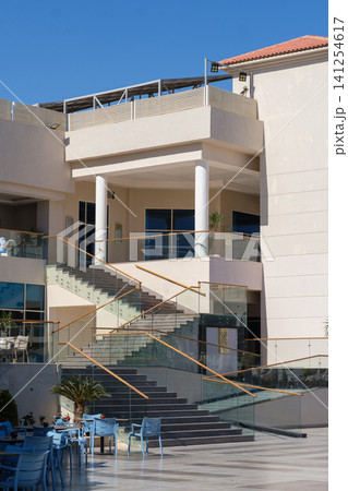 Modern commercial building architecture showcases a staircase with glass railings and outdoor seating area under bright sunlight 141254617