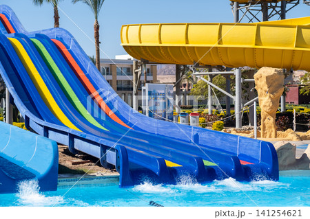 Colorful water slides in a water park feature a yellow slide and blue slides, splashing into a swimming pool under a bright blue sky Colorful water slides in a water park feature a yellow slide and blue slides, splashing into a swimming pool under a bright blue sky 141254621