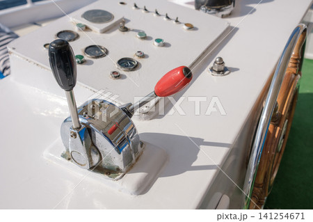 Boat control panel displays throttle lever, steering wheel, and gauges on a yacht's bridge, with a clear blue sky visible in the background 141254671