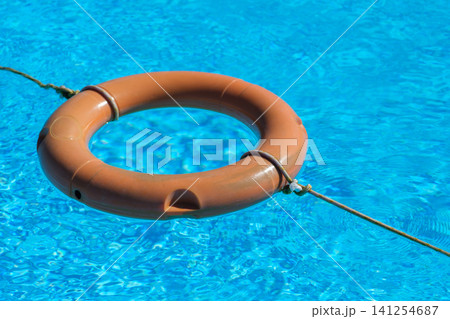 Orange lifebuoy is floating in clear blue water of a swimming pool, secured with a rope for safety and rescue applications Orange lifebuoy is floating in clear blue water of a swimming pool, secured with a rope for safety and rescue applications 141254687