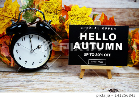 Hello Autumn Sale 30% off Special Offer text with alarm clock and maple leaf decoration on wooden background Hello Autumn Sale 30% off Special Offer text with alarm clock and maple leaf decoration on wooden background 141256843