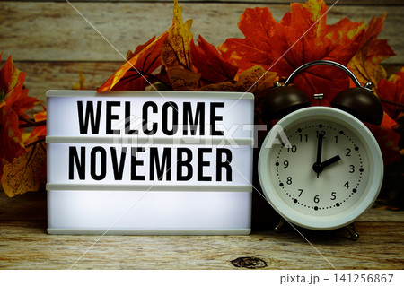 Welcome November text with alarm clock and maple leaf decoration on wooden background 141256867
