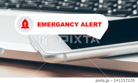 Emergency alert notification on smartphone displayed next to a laptop in a busy workspace during the day Emergency alert notification on smartphone displayed next to a laptop in a busy workspace during the day 141257229