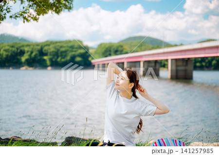 山と橋を望む湖畔でくつろぐ女性 山と橋を望む湖畔でくつろぐ女性 141257985