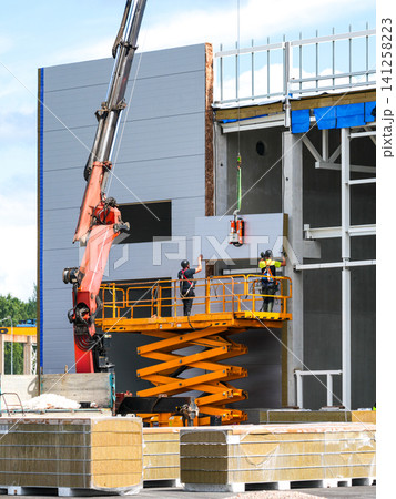 Installing Insulated Sandwich Wall Panels with Scissor Lift at Modern Industrial Building Construction Site Installing Insulated Sandwich Wall Panels with Scissor Lift at Modern Industrial Building Construction Site 141258223