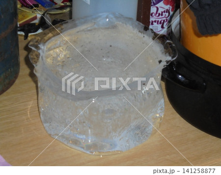 Ice block shaped by a bucket on wooden table, indoor close-up 141258877
