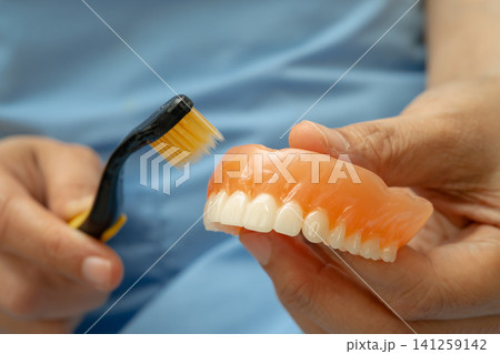 Asian senior woman patient clean teeth denture with toothbrush for chew food. Asian senior woman patient clean teeth denture with toothbrush for chew food. 141259142