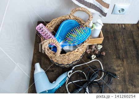 Bathroom Counter Organization with Woven Basket. Hairdryer, towel, curling iron and combs in the bathroom at home. Hairpins and hair care and styling items. Bathroom Counter Organization with Woven Basket. Hairdryer, towel, curling iron and combs in the bathroom at home. Hairpins and hair care and styling items. 141260254