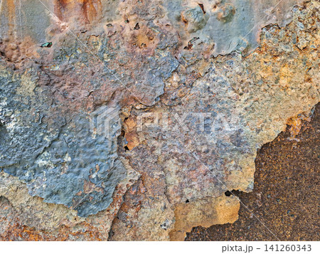 Close view of a heavily rusted metal surface stripped of blue paint in an old industrial area. The signs of wear and corrosion depict years of neglect. 141260343