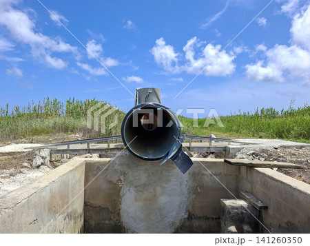 Looking through a large black irrigation pipe, the view shows a concrete channel in the rice fields of Pego. It is a clear day with some clouds in the sky. Looking through a large black irrigation pipe, the view shows a concrete channel in the rice fields of Pego. It is a clear day with some clouds in the sky. 141260350