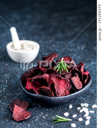 Homemade crispy vegan beet slices snack in a black bowl. Dark blue textured background with coarse sea salt, rosemary sprigs and copy space. Perfect for healthy diet and organic food marketing Homemade crispy vegan beet slices snack in a black bowl. Dark blue textured background with coarse sea salt, rosemary sprigs and copy space. Perfect for healthy diet and organic food marketing 141260374