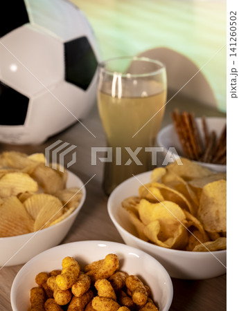 Soccer ball and assorted snacks on a table during a football match, capturing casual entertainment with food and relaxing drinks. 141260502