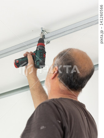 Construction worker using drill on metal frame for drywall suspended ceiling in apartment renovation 141260566