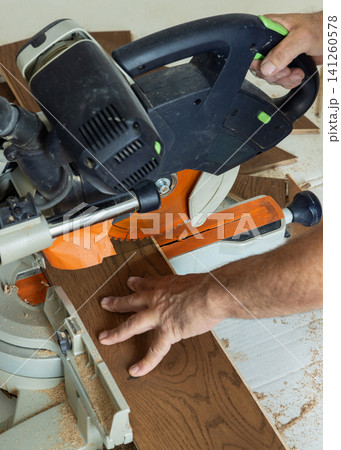 Construction worker cutting oak parquet planks with miter saw during hardwood floor installation Construction worker cutting oak parquet planks with miter saw during hardwood floor installation 141260578