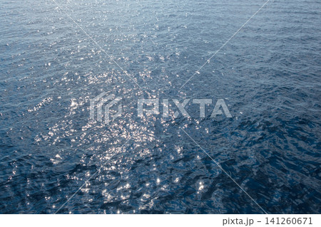Sunlight creates sparkling reflections on the surface of calm blue water, showcasing a tranquil and serene natural environment Sunlight creates sparkling reflections on the surface of calm blue water, showcasing a tranquil and serene natural environment 141260671