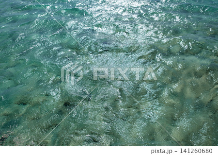 Clear turquoise water surface shows sunlight reflections and gentle ripples, with a sandy bottom and aquatic vegetation visible below Clear turquoise water surface shows sunlight reflections and gentle ripples, with a sandy bottom and aquatic vegetation visible below 141260680