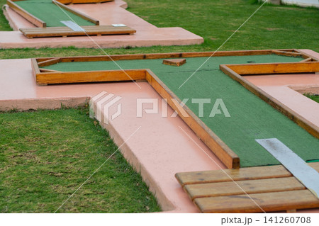 Miniature golf course design with green turf and wooden barriers, set on a manicured lawn in an outdoor recreational area Miniature golf course design with green turf and wooden barriers, set on a manicured lawn in an outdoor recreational area 141260708