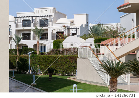 Modern residential architecture features balconies and palm trees in a well-maintained garden area under clear blue skies Modern residential architecture features balconies and palm trees in a well-maintained garden area under clear blue skies 141260731