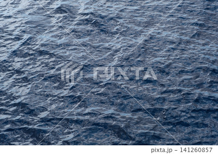 Dark blue water surface shows gentle ripples and reflections, creating a textured appearance in a natural aquatic setting Dark blue water surface shows gentle ripples and reflections, creating a textured appearance in a natural aquatic setting 141260857