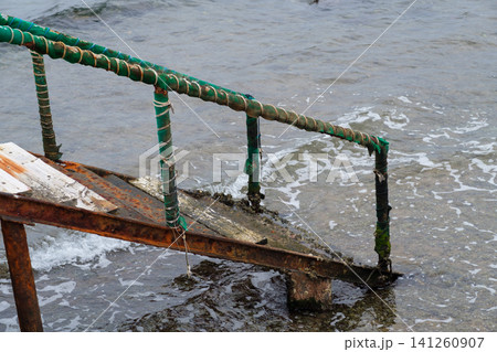 Weathered wooden staircase descends into the water, featuring green ropes and seaweed along the structure and surrounding shoreline 141260907
