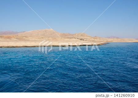 Coastal view with vibrant blue water and dry hills under a clear sky, highlighting the serene landscape and natural features of the region Coastal view with vibrant blue water and dry hills under a clear sky, highlighting the serene landscape and natural features of the region 141260910