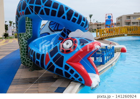 Colorful snake-shaped water slide features a vibrant design at a resort pool, with clear blue water and palm trees in the background Colorful snake-shaped water slide features a vibrant design at a resort pool, with clear blue water and palm trees in the background 141260924