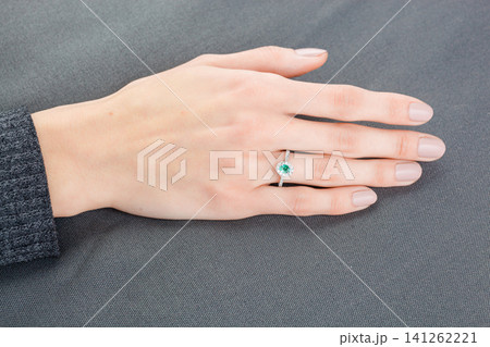 Beautiful female hand with gold ring with diamonds and emerald on gray background Beautiful female hand with gold ring with diamonds and emerald on gray background 141262221