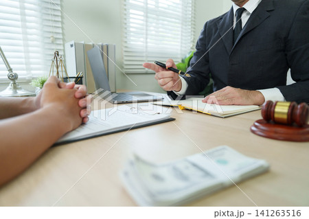 Lawyer explaining contract terms to client at desk with gavel and money 141263516