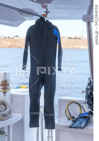 Black wetsuit suspended on a boat, accompanied by diving gear and an ocean view, highlighting water sports equipment and marine scenery 141264039