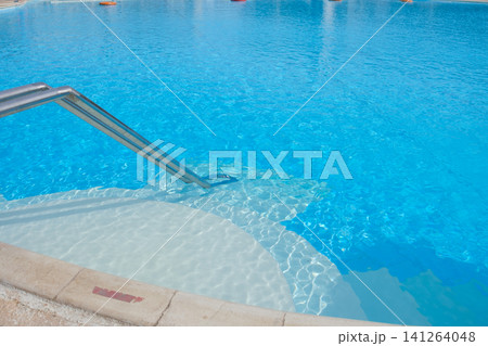 Swimming pool features clear blue water and a stainless steel ladder leading into the shallow end, with a concrete deck surrounding the area Swimming pool features clear blue water and a stainless steel ladder leading into the shallow end, with a concrete deck surrounding the area 141264048