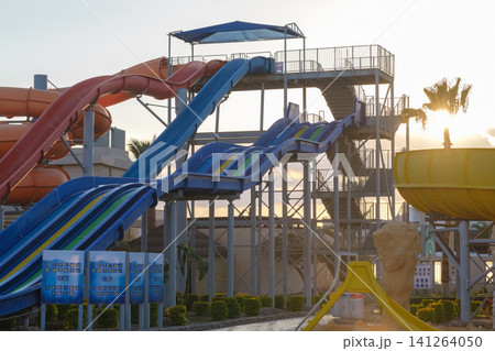 Water park scene showcasing vibrant water slides and a staircase, with palm trees and a bright sky visible in the background 141264050