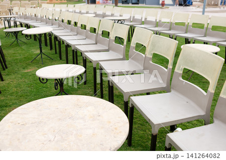Gray plastic chairs and round tables are neatly arranged on green grass in an outdoor area, suitable for events or social gatherings 141264082