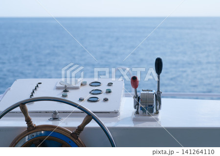 Boat steering wheel and control panel featuring throttle lever, with a clear view of calm ocean waters under bright daylight 141264110