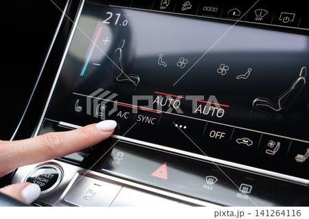 Woman finger pressing AC button on car touch screen climate control system Woman finger pressing AC button on car touch screen climate control system 141264116