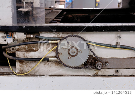 Close view of a mechanical chain drive sprocket and hydraulic hoses on machinery 141264513