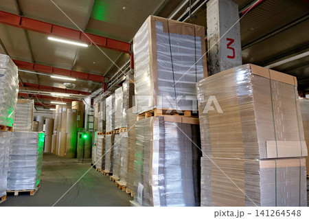 High stacks of cardboard material on wooden pallets stored in a spacious logistics warehouse facility 141264548