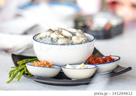 Fresh raw oysters sit on crushed ice inside a white ceramic bowl. Small dishes contain fried shallots garlic chili paste and green lead tree leaves. Fresh raw oysters sit on crushed ice inside a white ceramic bowl. Small dishes contain fried shallots garlic chili paste and green lead tree leaves. 141264612
